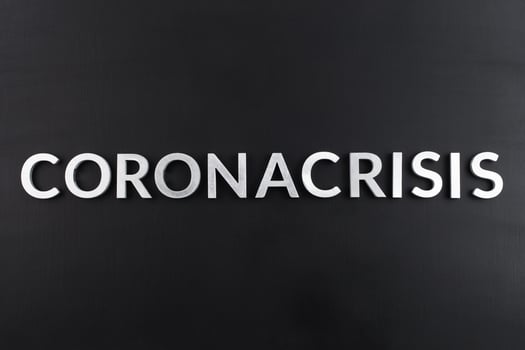the word coronacrisis laid with white brushed metal letters on flat black surface photo