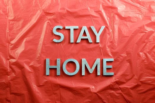 the words stay home laid with silver metal letters on crumpled red plastic background in flat lay perspective photo