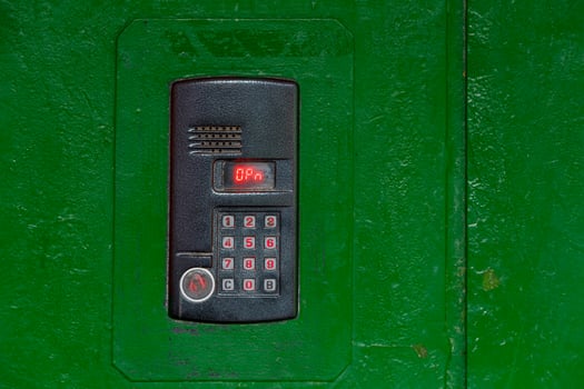 An intercom on green painted red steel surface with a keypad, digital display and rfid sensor for calling close-up photo