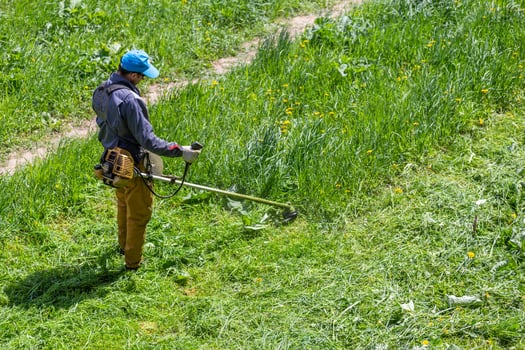 TULA, RUSSIA MAY 19, 2020 Russian official lawnmower worker man cutting green grass with two-cycle engine string trimmer. Top to down view. photo