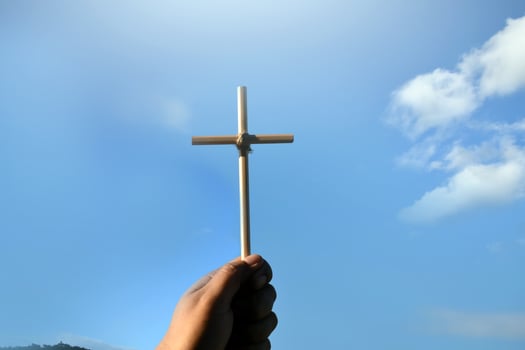 Small wooden cross holding in hand with cloudy and blue sky background, concept for love, hope, truth, faith, believe in Jesus, soft and selective focus. photo