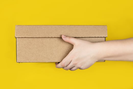 Large cardboard box in hands on a trendy yellow background. Horizontal photo. Concept - delivery of orders to your home by courier, receipt of parcels, safe distance photo