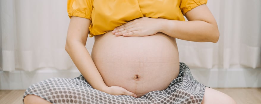 Young adult pregnant woman in white clothes touching big naked belly with hands. Showing shape. Pregnancy concept. Expectation time. Closeup. Isolated on light gray wall background. photo