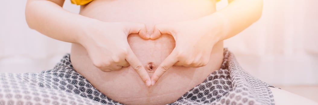 Young adult pregnant woman in white clothes touching big naked belly with hands. Showing shape. Pregnancy concept. Expectation time. Closeup. Isolated on light gray wall background. photo
