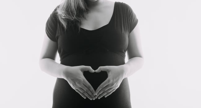 Young adult pregnant woman in white clothes touching big naked belly with hands. Showing shape. Pregnancy concept. Expectation time. Closeup. Isolated on light gray wall background. photo