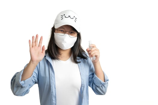 Asian young female in a casual blue t-shirt and white cap is spraying and washing her hand by a small alcohol spray bottle on her hand. white clear background studio light. photo