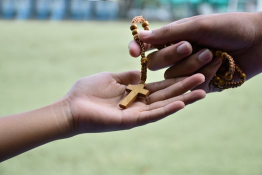 Closeup hands which offering wooden cross bead rosary to other people concept, soft and selective focus. photo