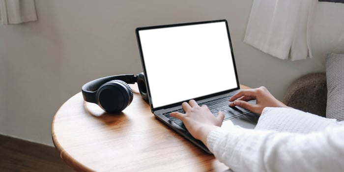 Girl typing on laptop with blank screen,  headphones on wooden table, mock up photo