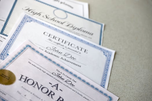 A honor roll recognition, certificate of achievement and high school diploma lies on table. Education documents photo