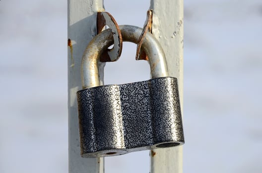 A large gray padlock hangs on a metal gate photo
