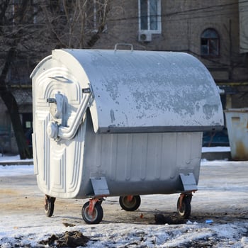 A silver garbage container stands near residential buildings in winter photo