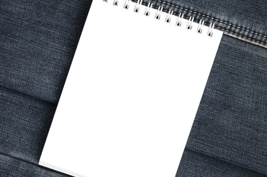 White notebook with clean pages lying on dark blue jeans background. Image with copy space photo