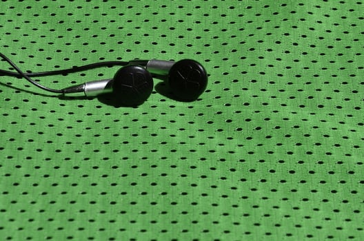 Black earphones lie on the green sportswear of polyester nylon fiber. The concept of listening to music during sports training with modern technology photo