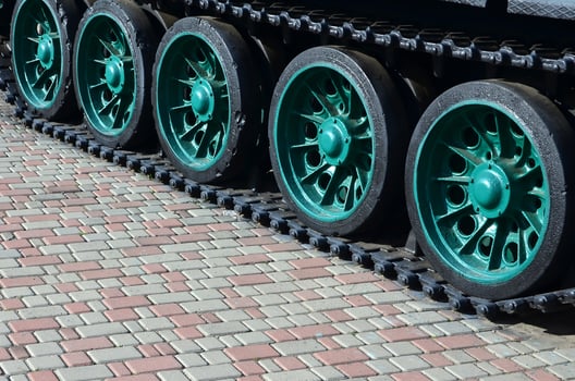 A military vehicle on caterpillar tracks stands on a square of paving stones. Photo of green caterpillars with metal wheels that rotate them