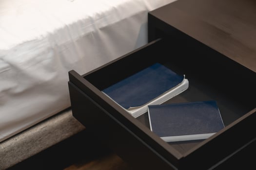 Bed with white sheet and next to wooden drawer stand and note book inside. photo