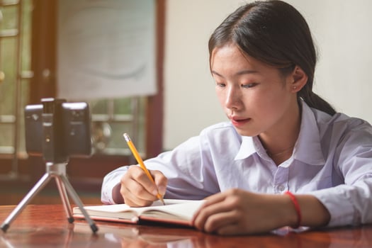 A women student with student suit is studying online from mobile phone at home with teacher, note teacher's explain knowledge on his book, education and online learning concept copy space for text photo