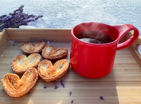 Red mug with cookies on the snowred ceramic cup with hot tea and puff pastry sugar cookies in the shape of hearts on a wooden tray, on snow on a sunny day, out of focus background, concept of love photo