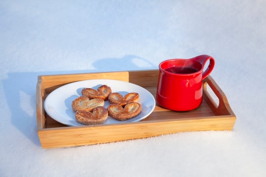 Red mug with cookies on the snow red ceramic cup with hot tea and puff pastry sugar cookies in the shape of hearts on a wooden tray, on snow on a sunny day, out of focus background, concept of love, photo