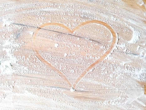 Heart drawn by finger with flour on wooden table photo
