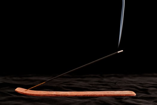Smoke curls of burning incense stick in wooden holder for relaxation and meditation black background photo