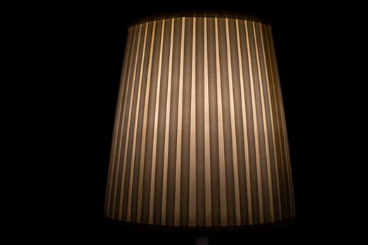 Lampshade lamp. Lamp is in dark. Light on black background. Ribbed paper. photo