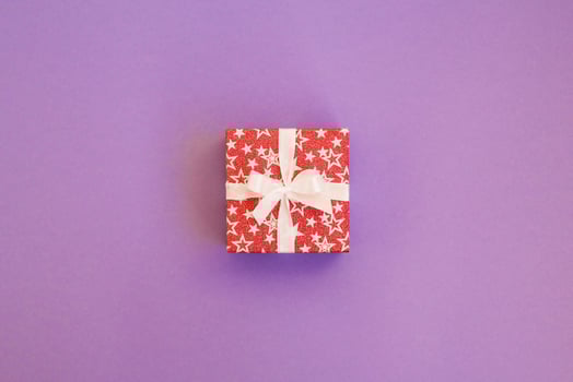 Gift box wrapped in red shiny paper with white ribbon on purple background. Mockup with copy space. photo