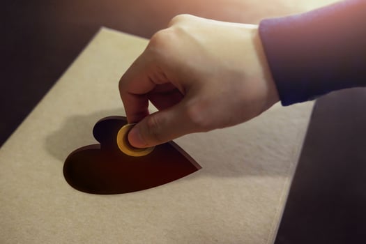 Donation Concept. Hand putting Money Coin into a Heart Shape hole on Donate Box photo