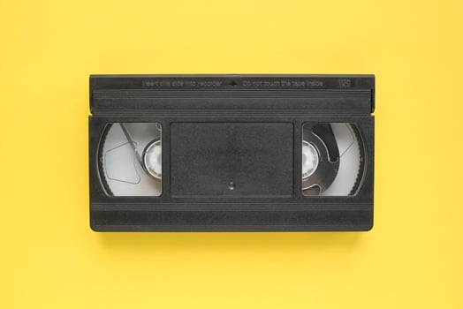 Black VHS videotape recorder cassette on yellow background. Old obsolete technology for tape recording and watching media movies. Retro, vintage, history, nostalgia concept. Top view, flat lay photo
