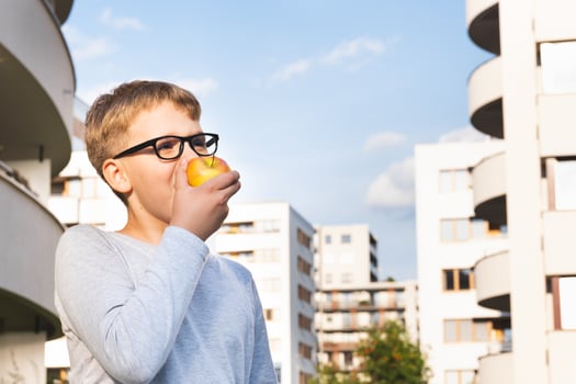 Cute schoolboy with glasses eating apple against the blue sky on a sunny day. photo