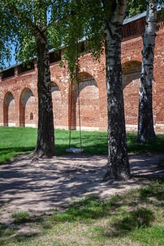 Wooden swing on chains between trees in free flight against the background of the old brick Kremlin wall, Zagorsk Russia. The concept of travel, healthy lifestyle photo