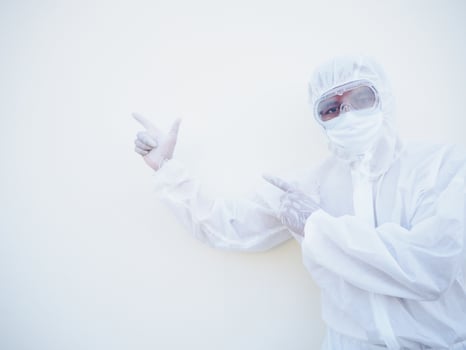 Asian male doctor or scientist in PPE suite uniform showing pointing two fingers away at copy space while standing and looking forward. coronavirus or COVID-19 concept isolated white background photo