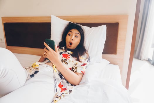 Shocked young woman checking on her phone while lying in bed photo