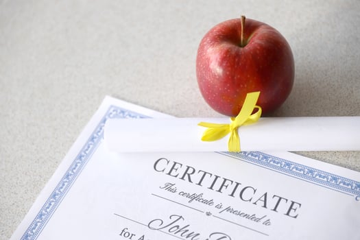 A certificate of achievement lies on table with small scroll and red apple. Education documents photo