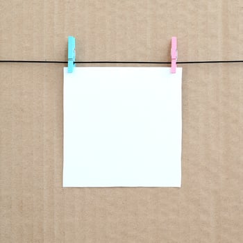 White blank card on rope on a brown cardboard background. Creative reminder, small sheet of paper on wooden clothespin, memo backdrop photo