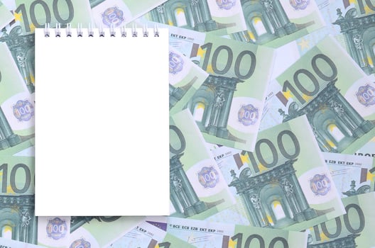 White notebook with clean pages lying on a set of green monetary denominations of 100 euros. A lot of money forms an infinite heap photo