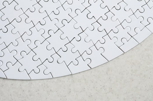 A white jigsaw puzzle in the complete form lies on a treated stone surface. Textured image with copy space photo