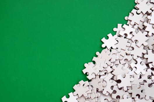 A pile of uncombed elements of a white jigsaw puzzle lies on the background of a green surface. Texture photo with copy space for text