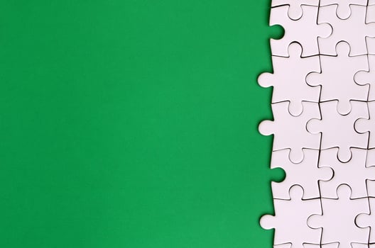 Fragment of a folded white jigsaw puzzle on the background of a green plastic surface. Texture photo with copy space for text