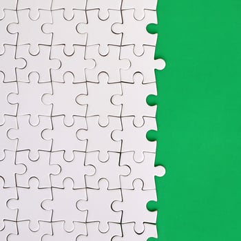 Fragment of a folded white jigsaw puzzle on the background of a green plastic surface. Texture photo with copy space for text