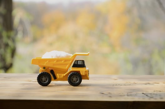 A small yellow toy truck is loaded with a stone of white salt. A car on a wooden surface against a background of autumn forest. Extraction and transportation of salt photo