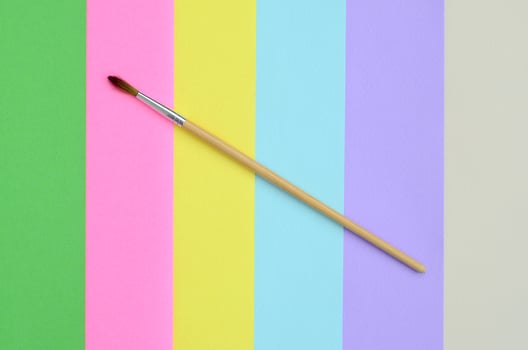 A new paint brush lie on texture background of fashion pastel pink, blue, green, yellow, violet and beige colors paper in minimal concept. Abstract trendy pattern photo