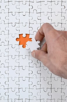 The texture of a white jigsaw puzzle in the assembled state with one missing element that the male hand puts in photo