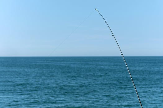 Fishing rod against blue ocean or sea background, copy space. Waiting for biggest haul. Meditative relax sport. photo