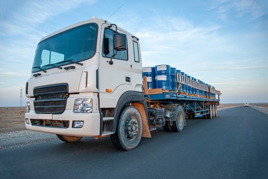 A dump truck with metal barrels on the road against a beautiful sky photo