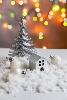 Abstract Advent Christmas Background. Toy model house and winter decorations ornaments on background with snow and defocused garland lights. Christmas with family at home concept. photo