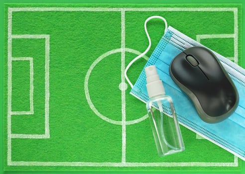 Computer mouse and sanitizer with blue medical mask placed on mini football field made of green felt, top view. Concept stay home, protect yourself from coronavirus and watch match broadcast online. photo