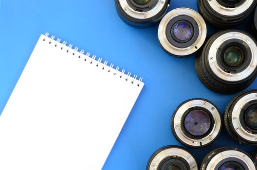 Several photographic lenses and white notebook lie on a bright blue background. Space for text photo