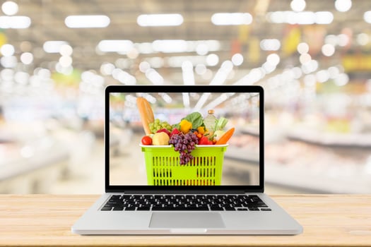supermarket aisle blurred background with laptop computer and shopping basket on wood table grocery online concept photo