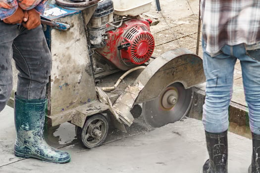 Worker using diamond saw blade machine cutting concrete road at construction site photo