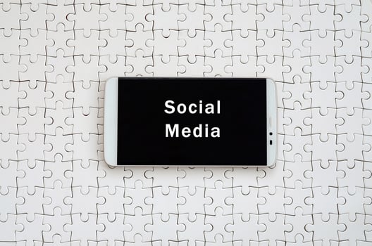 A modern big smartphone with a touch screen lies on a white jigsaw puzzle in an assembled state with inscription. Social media photo
